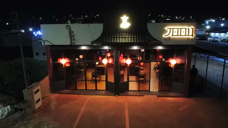 Fachada da JOOU à noite, vista de cima, com o letreiro iluminado e as lanternas no salão