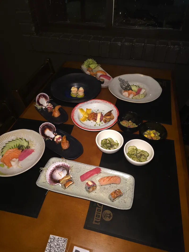 Mesa da JOOU com várias etapas da Sequência: sashimis, niguiris, vieira na concha e entradas